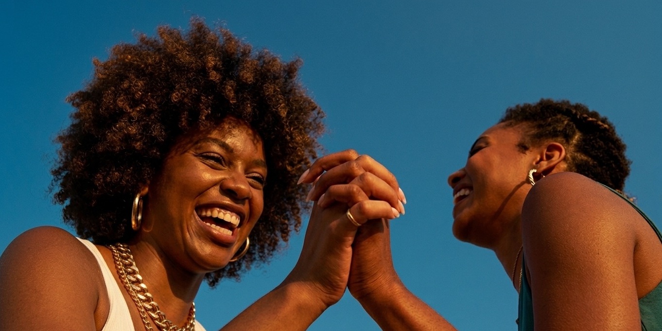 Two friends celebrating together against a clear blue sky